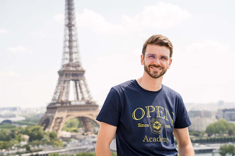 Un grand à lunette avec un tee-shirt bleu dos à la Tour Eiffel